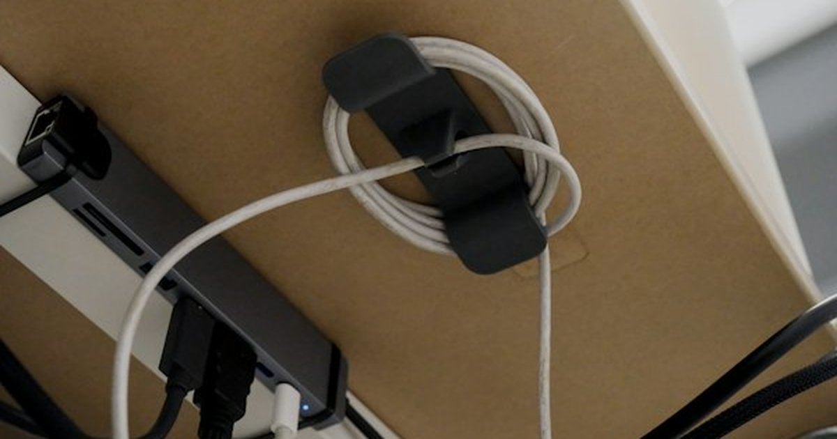 Under-desk cable management organizer clip holding coiled wire and power dock beneath tabletop