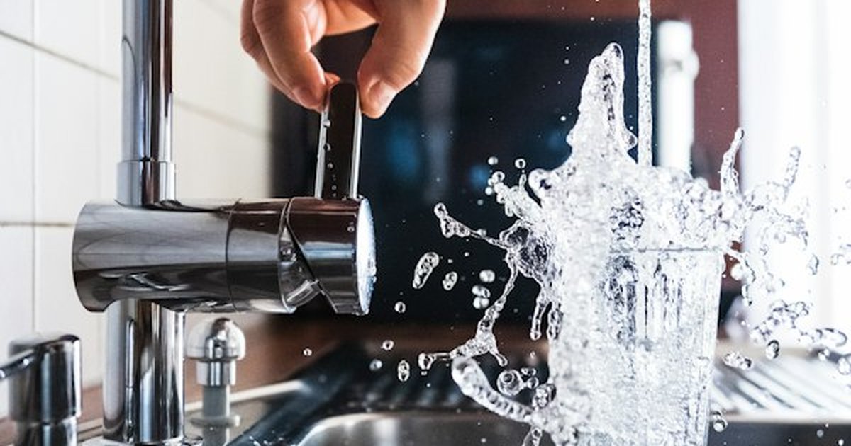 Clean kitchen tap water splashing into drinking glass representing domestic point-of-use filtration