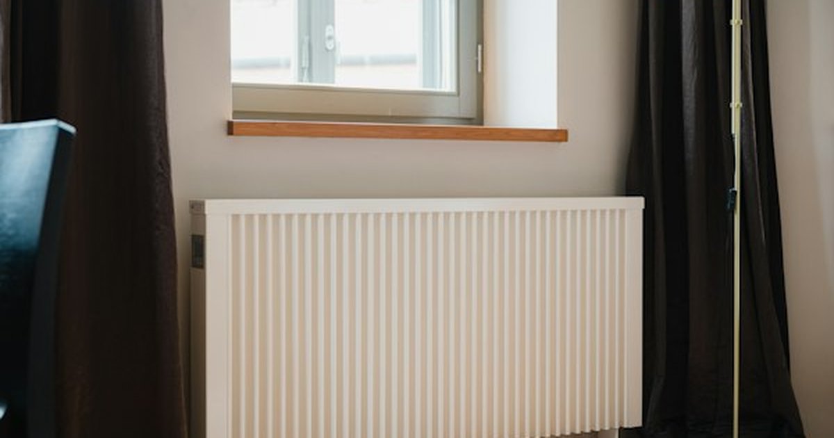 White wall-mounted residential radiator heater positioned beneath window drapery