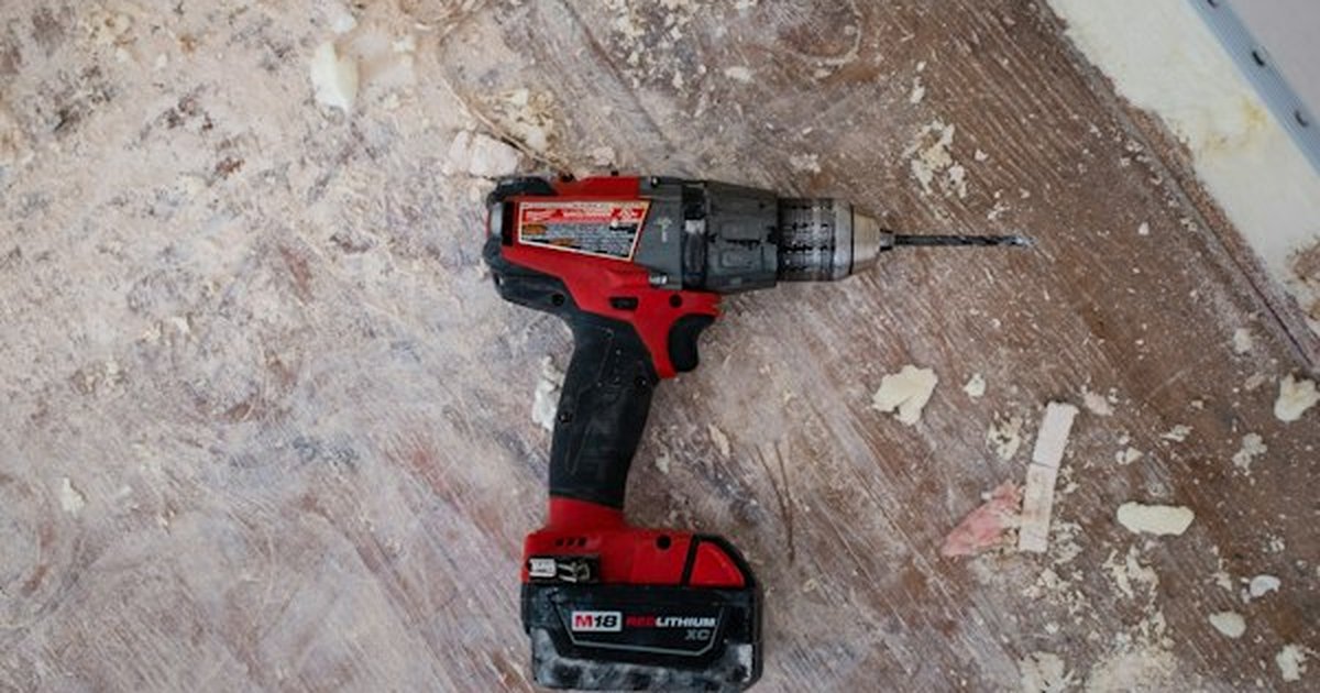 Cordless power drill, drill bit, and fasteners resting on drywall subfloor ready for shelf mounting