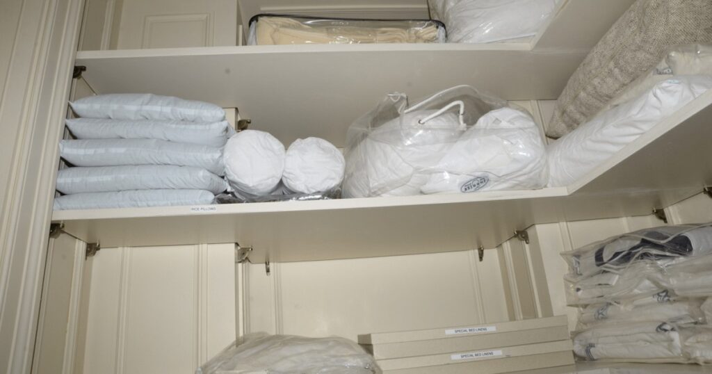 Well-organized linen closet with labeled storage shelves and folded bedding in protective covers