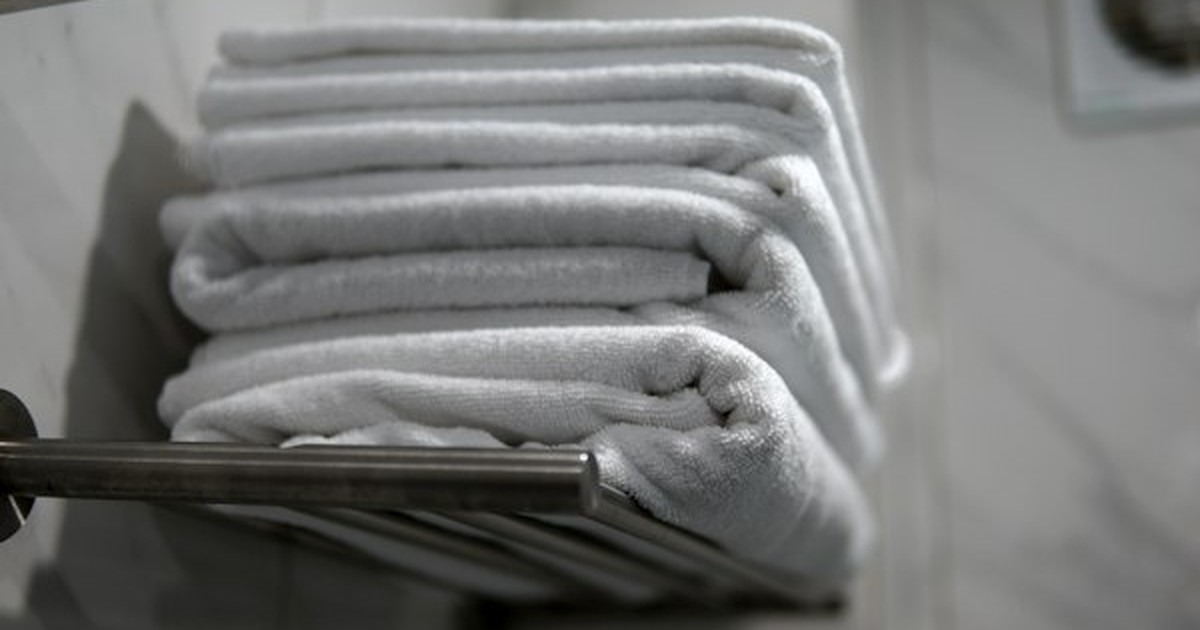 Neatly folded stack of white bath towels arranged horizontally on shelving rack