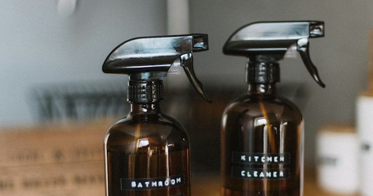 Refillable amber glass spray bottles labeled for bathroom and kitchen cleaners on counter